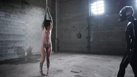 Two brunette women in latex dominate man in dungeon