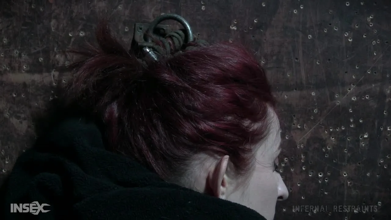Redhead in metal restraints on concrete floor with pink device play