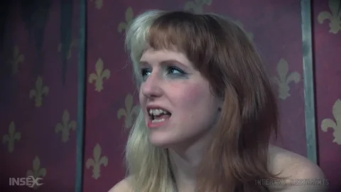 Blonde with brown roots gagged and pinned under wooden blocks on red w